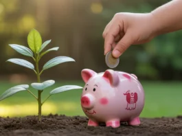 Vaiko ranka deponuoja monetą į kiaulės banką, šalia jo auga mažas augalas.